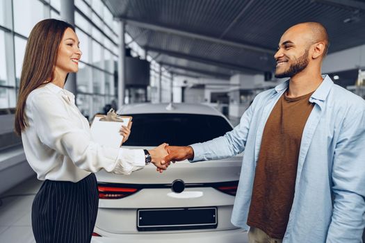 Woman car seller and man car buyer handshaking in car salon