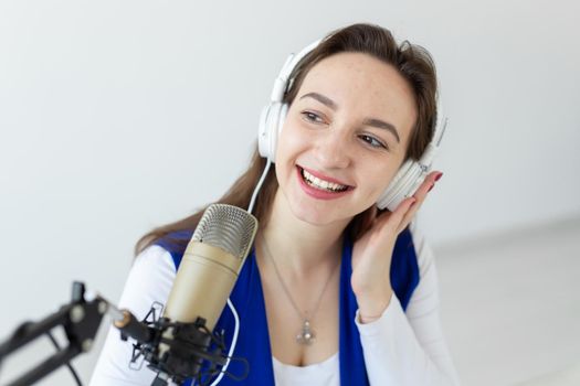 Radio host concept - Woman working as radio host sitting in front of microphone over white background in studio
