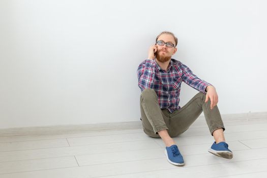 Bearded man sitting on the floor and talking on the phone, light background with copy space