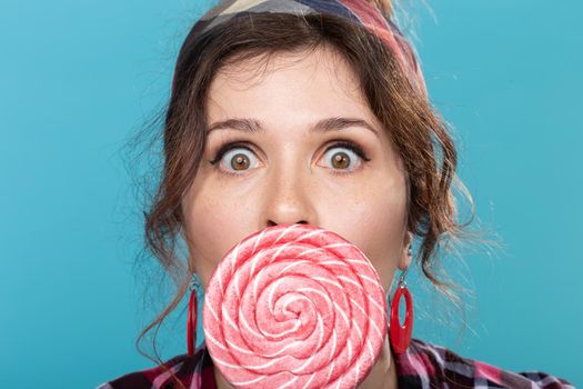 candy, diet and junk food concept - portrait of surprised pin-up woman with big lollipop on blue background