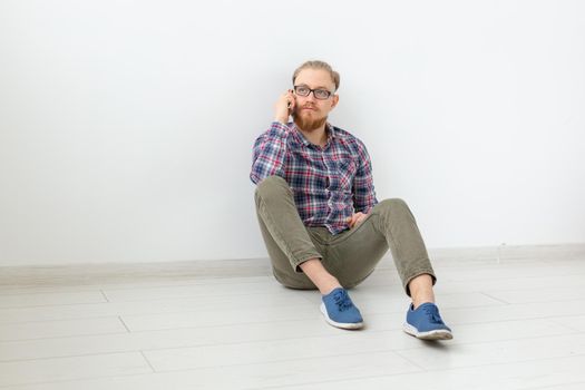 Bearded man sitting on the floor and talking on the phone, light background with copy space