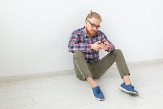 Bearded man sitting on the floor with phone, light background with copy space