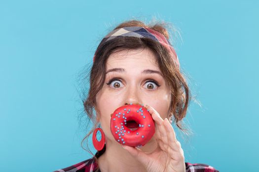 Junk food, diet and unhealthy lifestyle concept - pin-up woman closed her mouth by doughnut