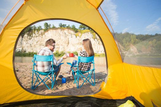 people, summer tourism and nature concept - young couple resting near camping tent