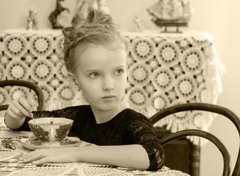 Beautiful little girl drinking tea at the table.