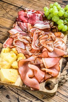 Meat antipasto board, pancetta, salami, sliced ham, sausage, prosciutto, bacon with grape and parmesan cheese. Wooden background. Top view
