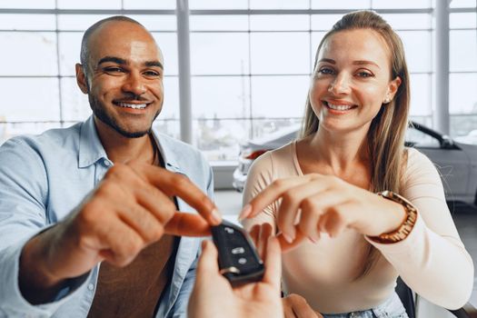 Cheerful couple taking keys of their new car in car dealership