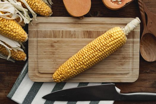 Corn cob and pumpkin on brown wooden board