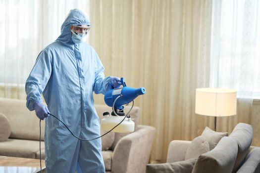 Man wearing protective clothes with disinfectant in hotel room