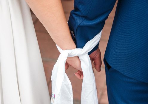 The bound hands of the bride and groom holding together tightly close up
