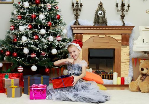 Little girl sitting near Christmas tree with a big gift.