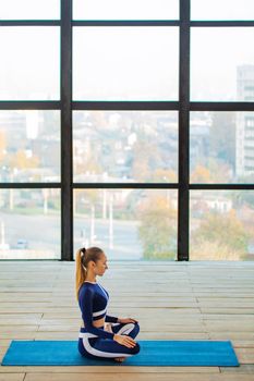Yoga asana Indoor before a large panoramic window. Sports recreation. Beautiful young woman in yoga pose. Individual sports.