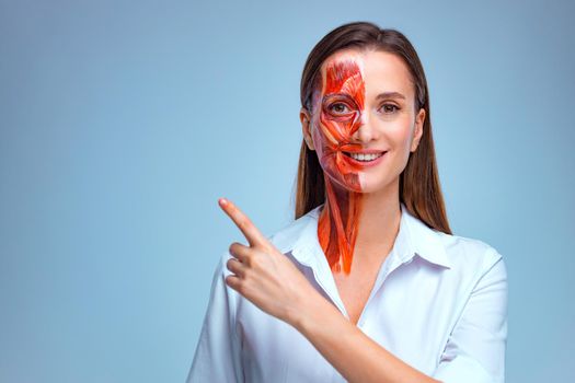Cosmetology concept. Young woman with half of face with muscles structure under skin pointing to looking left on copy space.. Model for medical training on a light background