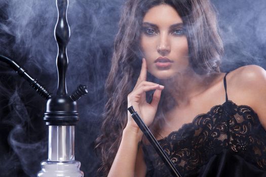 Young, beautiful woman in the night club or bar smoke a hookah or shisha. The pleasure of smoking. Sexy smoke.