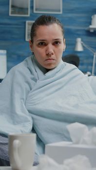 Woman with virus infection sitting in blanket looking at camera