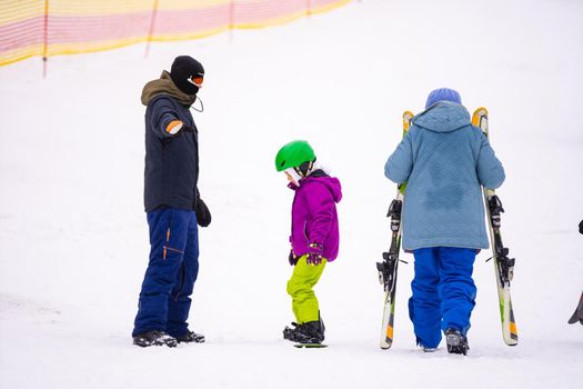 Instructors teach a child on a snow slope to snowboard