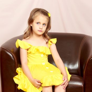 A little girl is sitting on a leather chair.