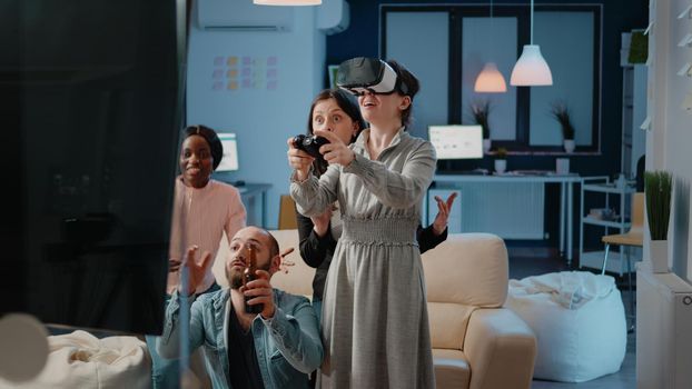 Woman using joystick and vr glasses while workmates cheering