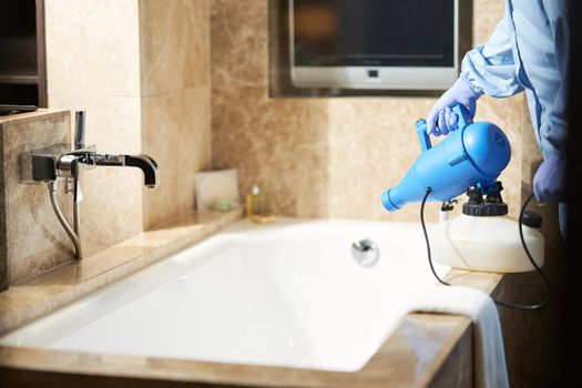 Technician in protective clothing sanitizing a hotel bathroom