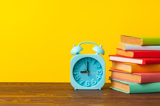 Books and alarm clock on wooden table, education concept
