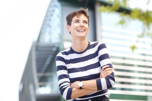 confident young woman laughing outdoors with arms crossed