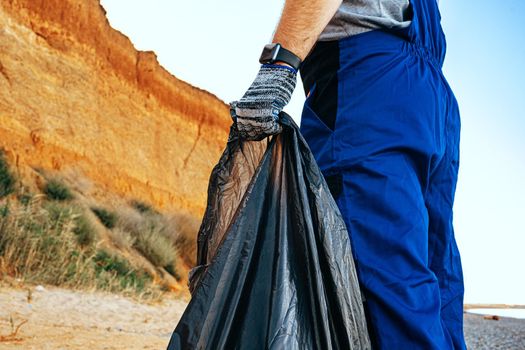 Volunteer man standing on the beach with a full bag of collected trash