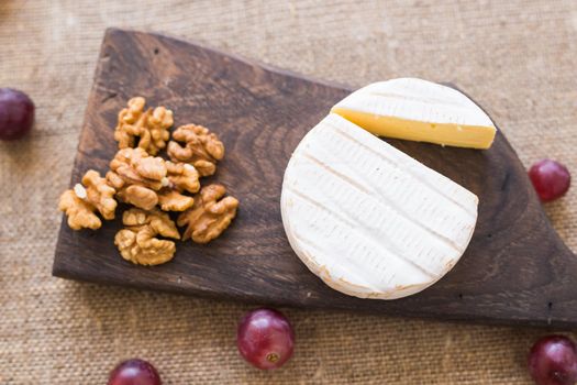 Brie or camembert cheese with nuts and grapes on a wooden board top view