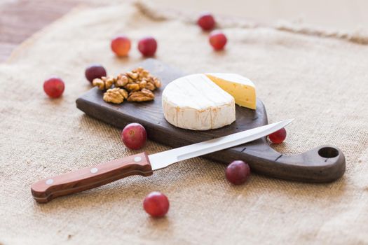 Brie or camembert cheese with nuts and grapes on a wooden board