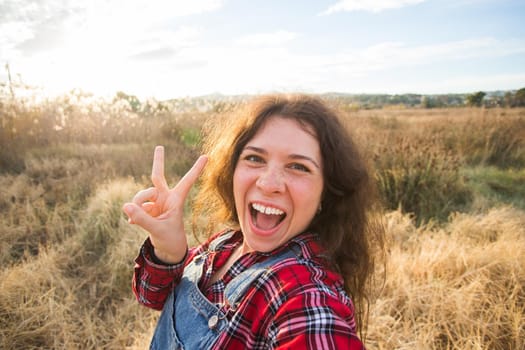 Travel, tourism and nature concept - Young woman fooling around taking selfie on field