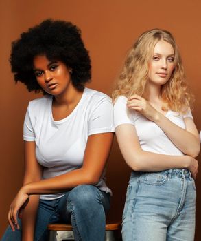 young pretty african and caucasian women posing cheerful together on brown background, lifestyle diverse nationality people concept