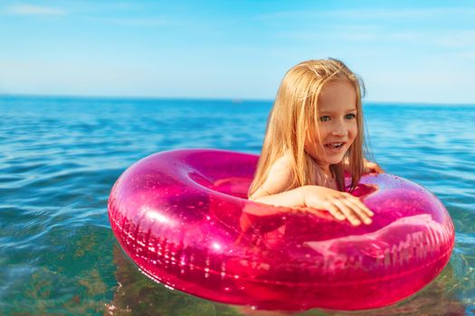 Little girl with pink inflatable circle bathing in sea