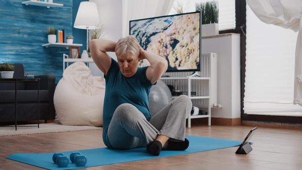 Senior adult doing physical exercise and watching video on tablet