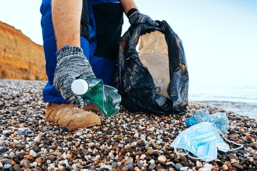 Hand of a man volunteer grabbing plastic litter into a waste bag cleaning up the beach