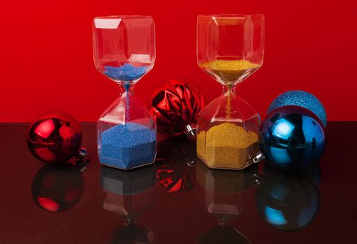 Hourglass and Christmas balls against red background
