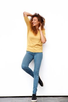 Full body happy young woman with hands in curly hair against white wall
