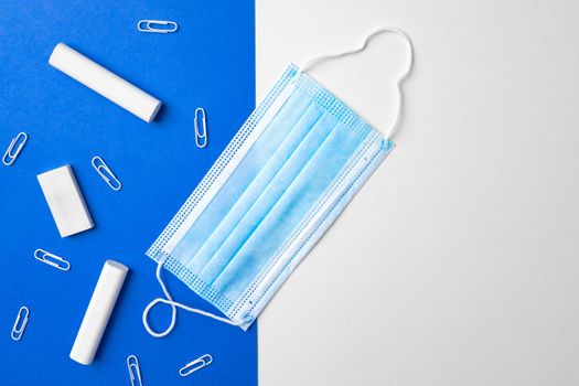 Pieces of chalk, paper clips and medical mask on blue and white background