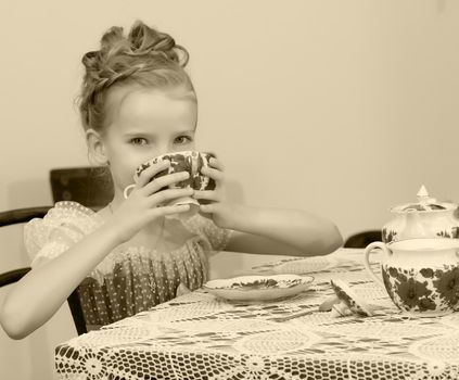 Cute little girl drinking tea at the old table.