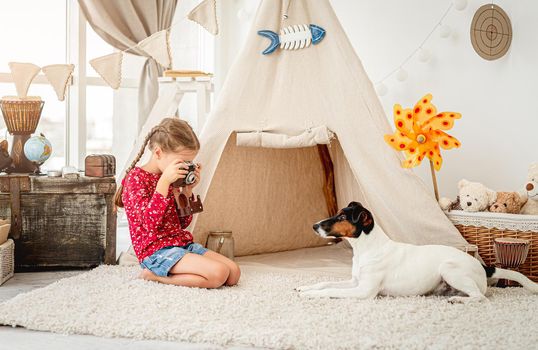 Little girl photographing fox terrier indoors