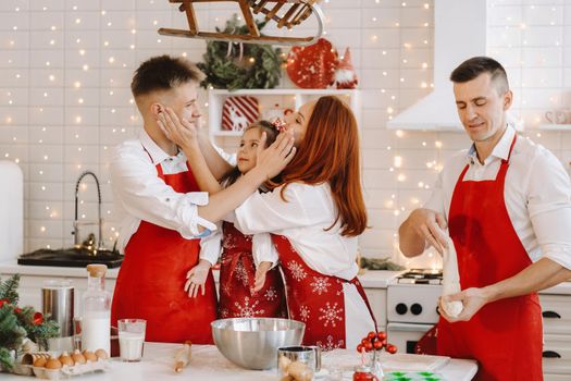 A happy family is standing in the Christmas kitchen and smearing each other with flour