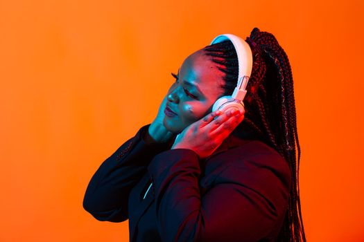 African american young woman listening to music online dancing and singing with headphones, neon light. Music and technology concept.