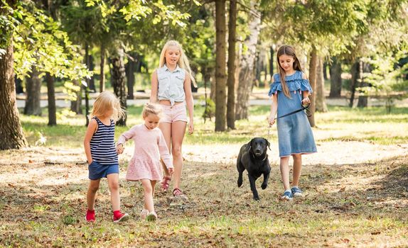 Little girls walking with a black dog in a park