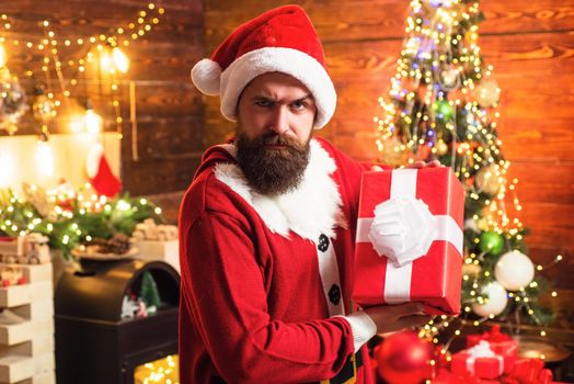 Delivery gifts. Gift emotions. Santa man holding gift. Hipster in red Santa hat holding present. Bearded santa.