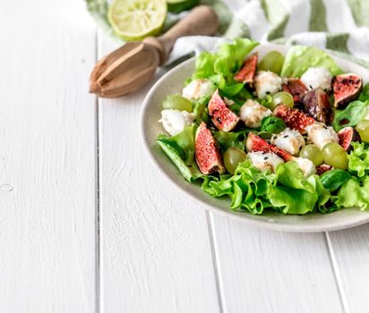 Salad with figs, mozzarella and grapes on a white wooden background.