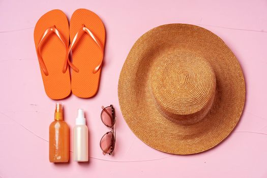 Suntan oil spray bottles and straw hat on pink background