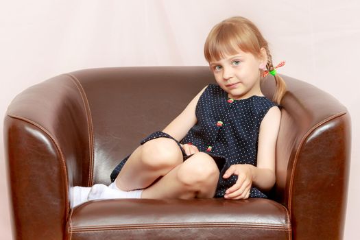 A little girl is sitting on a leather chair.