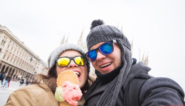 Travel in winter and Italy concept - Happy young couple take selfie photo with ice-cream in front of Milan Duomo Cathedral.