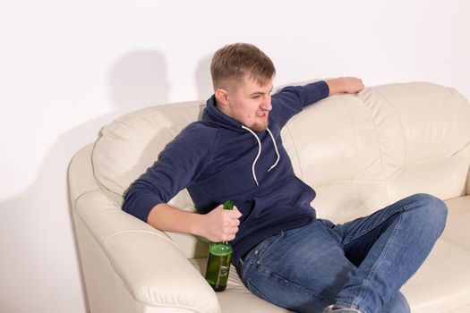 Depression and alcoholism concept - Aggressive male alcoholic sitting on the sofa