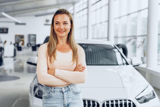 Pretty young woman standing near new car in car showroom