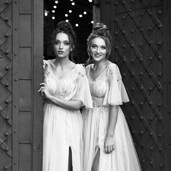 Beautiful retro styled bridesmaids ladies in gorgeous elegant stylish light grey silver floor length dresses in old beautiful European city welcome greeting guests at the gate. Black and white.