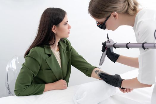 Beautician using laser device to remove an unwanted tattoo from female arm. Concept of erasing tattoos as an expensive procedure in a cosmetology clinic